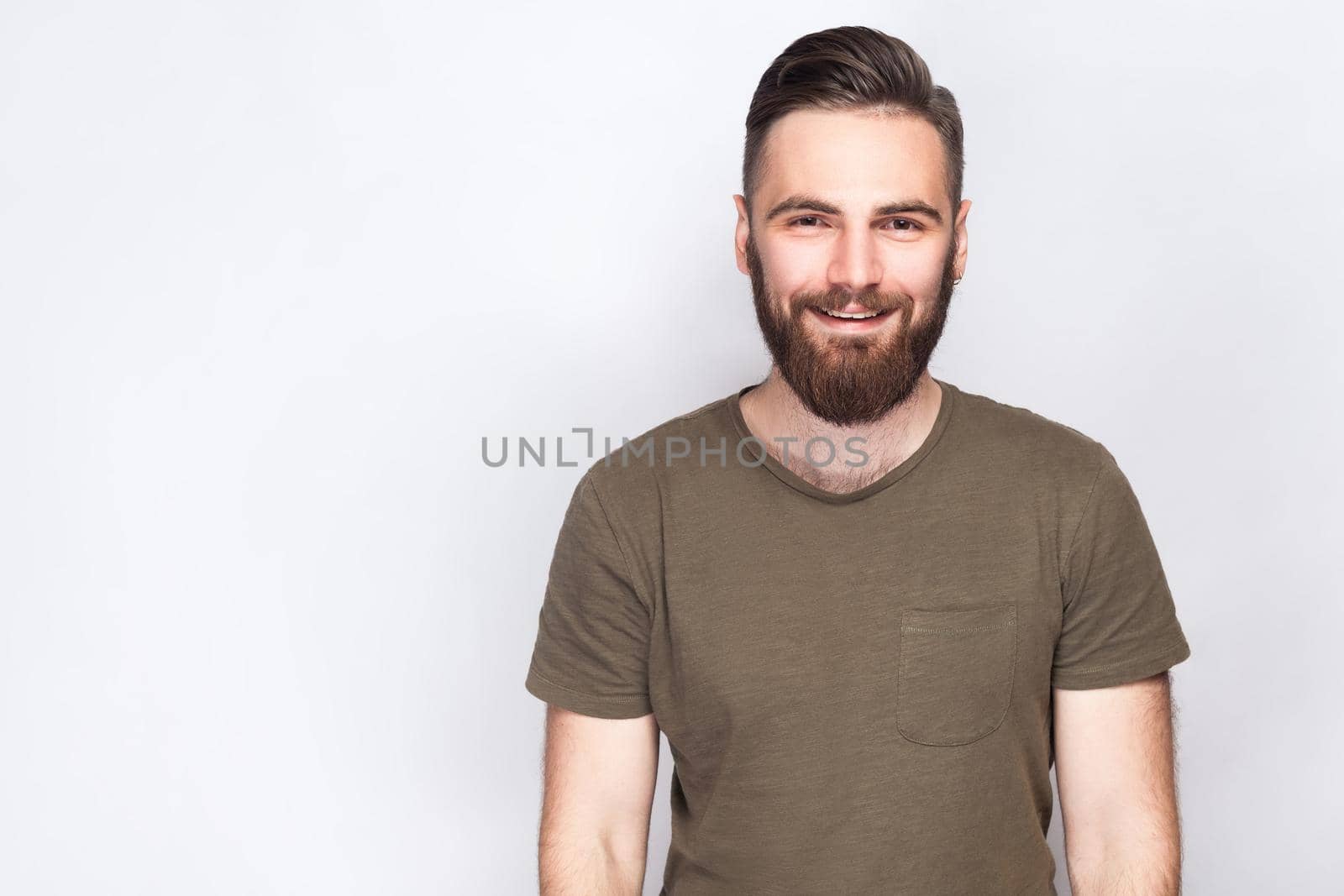 Portrait of happy smiley bearded man with dark green t shirt against light gray background. studio shot. .