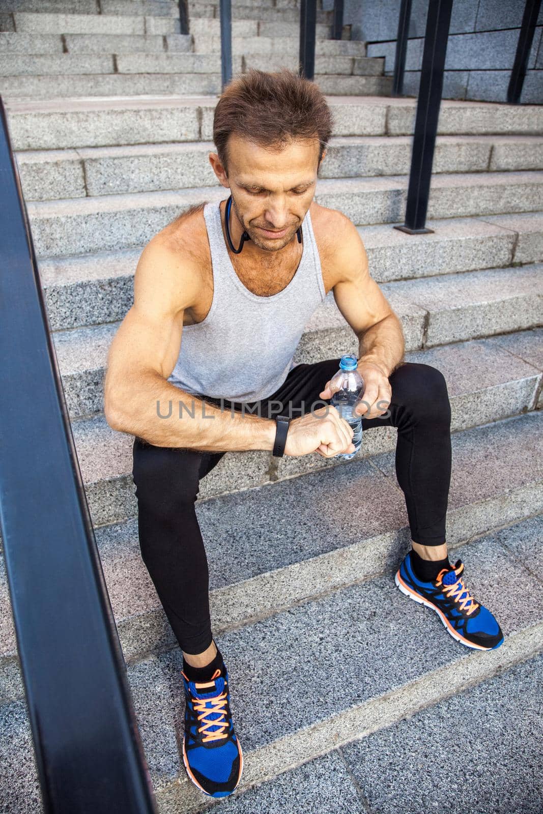 Sportsman with bottle of water is resting and checking his smart watch after running. fitness, sport, exercising and people healthy lifestyle concept.