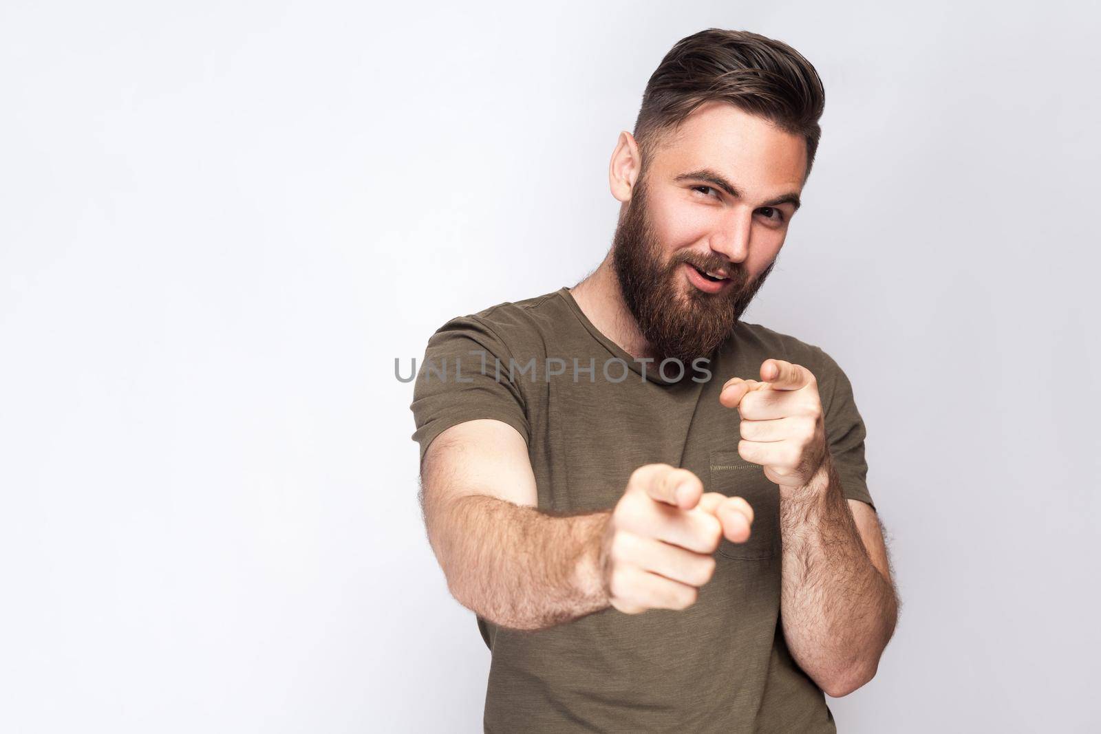 Hey you! Portrait of happy bearded man with dark green t shirt against light gray background. studio shot. .