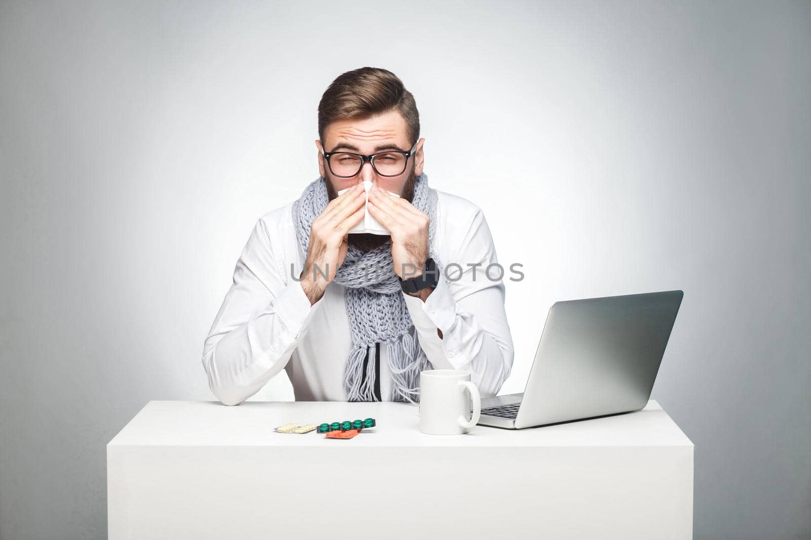 Portrait of sick scribble young boss in white shirt, scarf and black tie are sitting in office and need to finish important report, have grippe virus. Studio shot, isolated, gray background, indoor