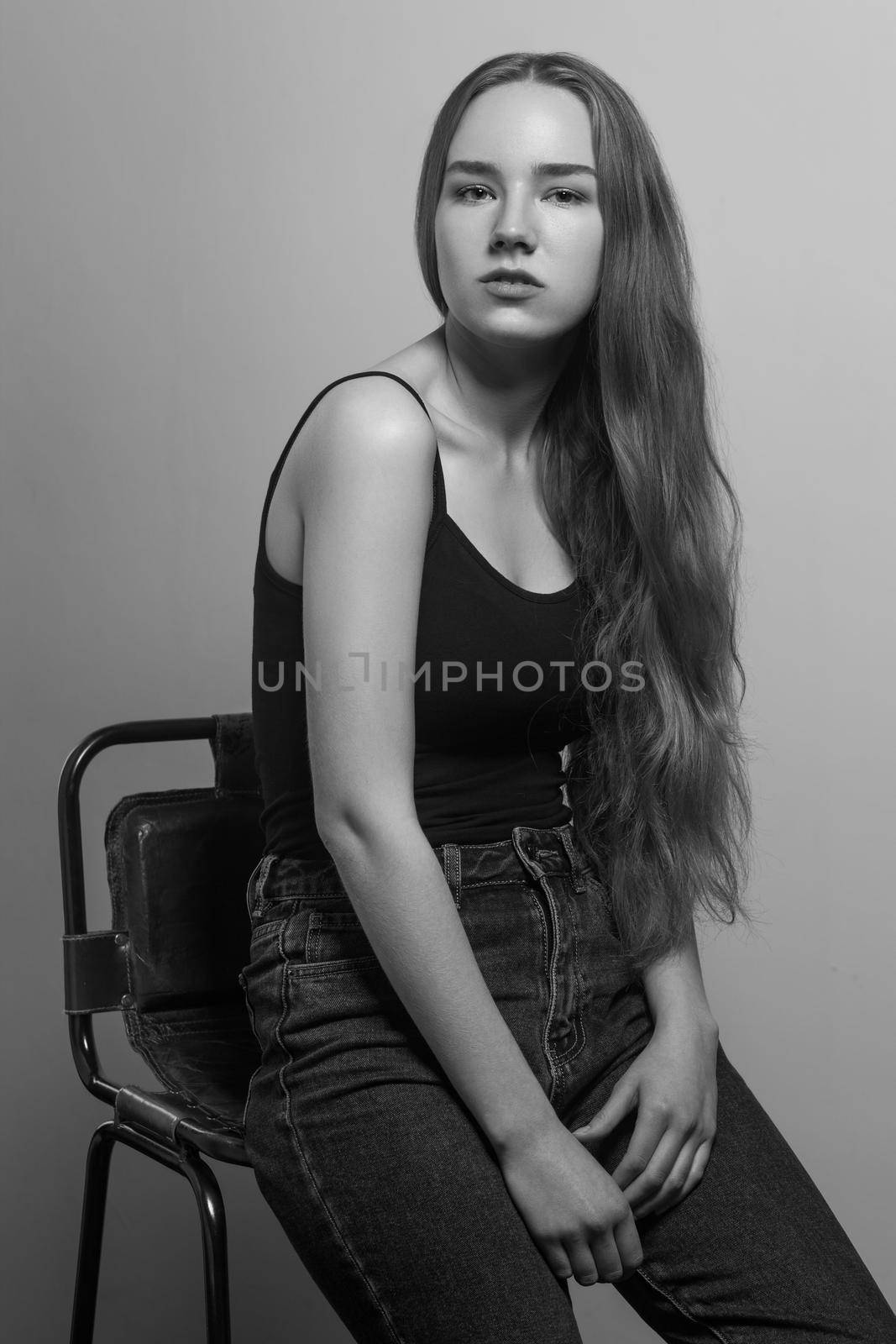 Gesture woman sit on chair and looking at camera. Studio shot, isolated on gray background