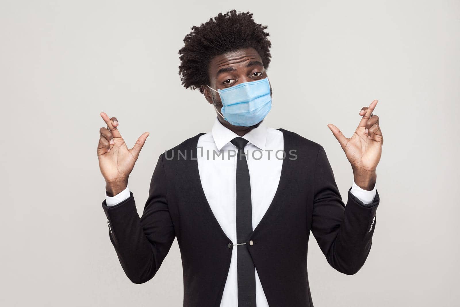 handsome worker man in black suit with surgical medical mask standing with crossed fingers and hope. by Khosro1