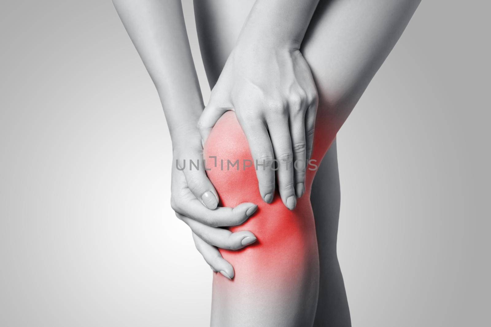 Closeup view of a young woman with knee pain on gray background. Black and white photo with red dot.