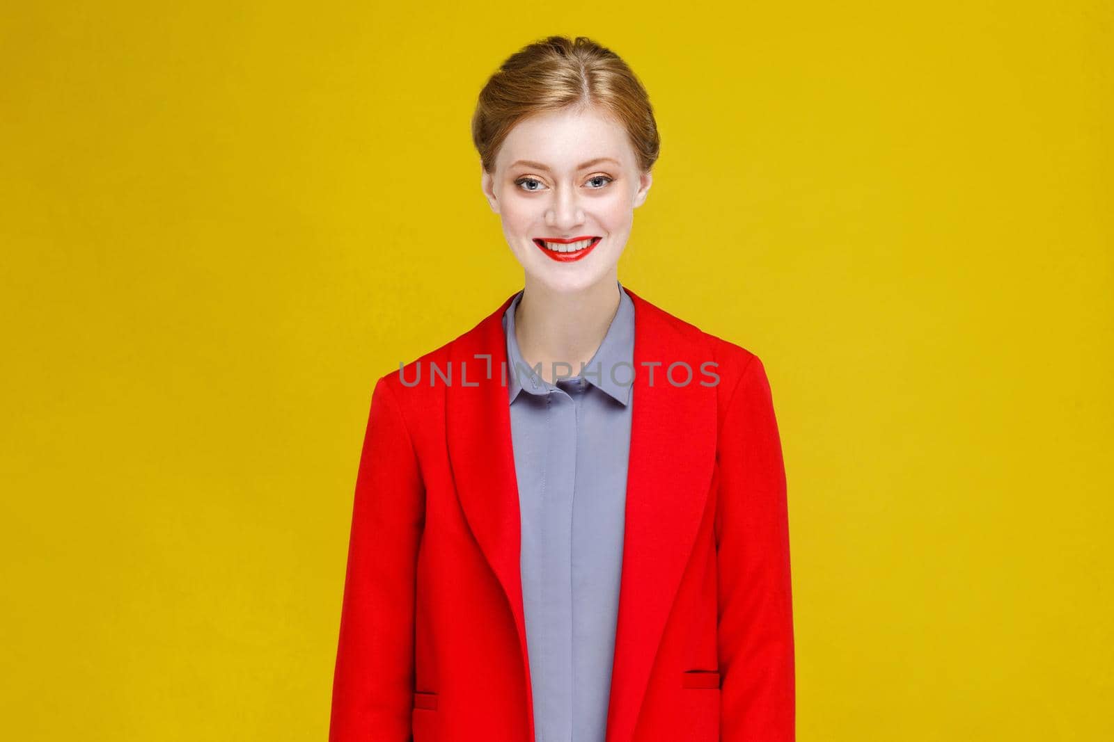 Funny happiness red head model in red suit toothy smile. Studio shot, isolated on yellow background