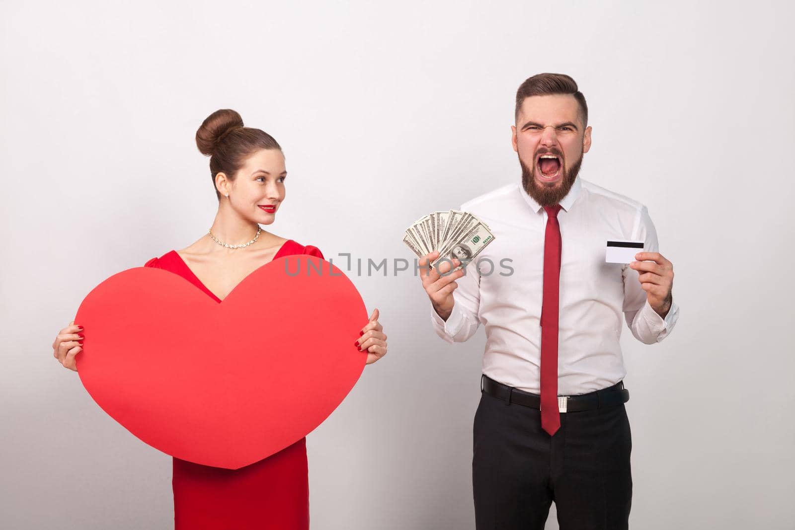 Angry man roar, his pays for love, woman smiling. Indoor, studio shot, isolated on gray background