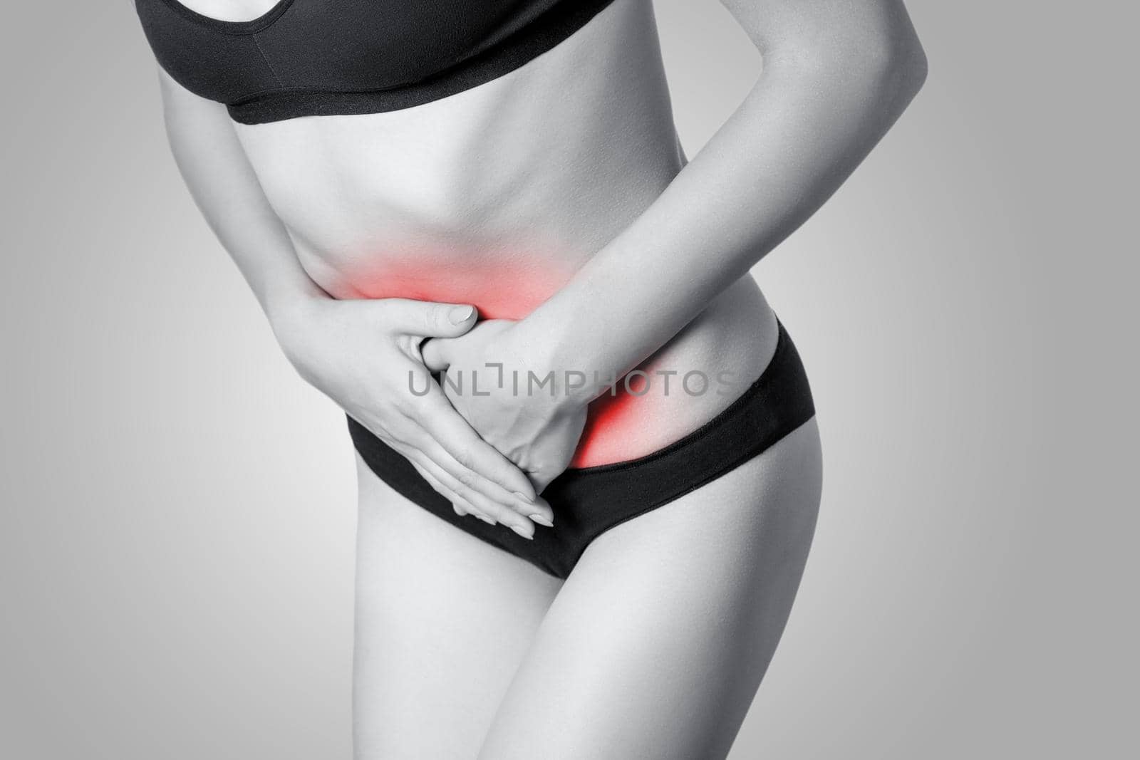 Closeup view of a young woman with stomach pain or digestion or period cycle on gray background. Black and white photo with red dot.