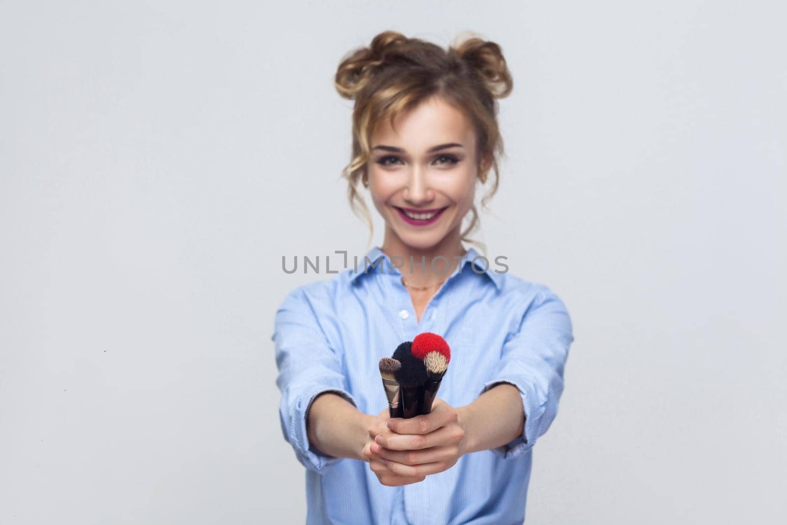 Focus on brush. Happiness young adult girl showing brush at camera and smiling. Studio shot