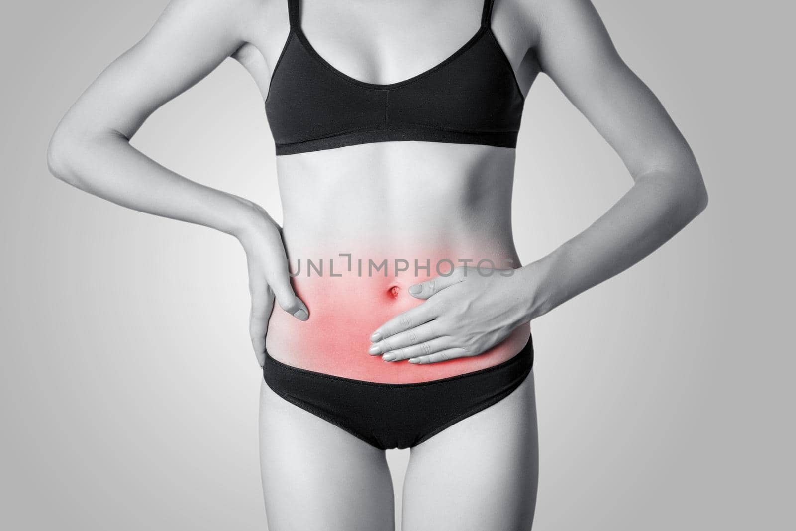 Closeup view of a young woman with stomach pain or digestion or period cycle on gray background. Black and white photo with red dot.