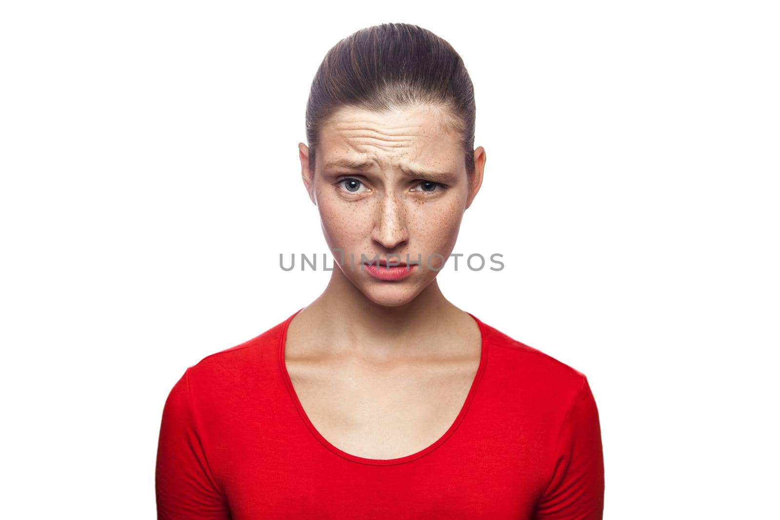 I don't know. portrait of funny confused woman in red t-shirt with freckles. looking at camera, studio shot. isolated on white background.