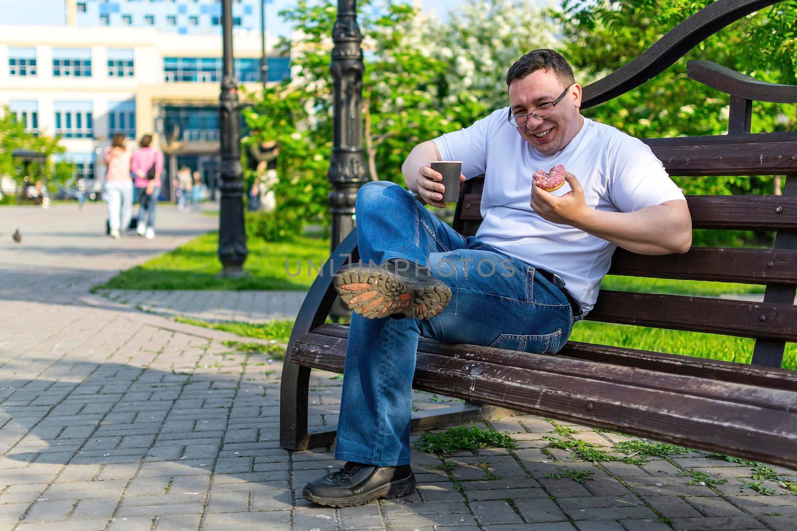 A cheerful young man, sitting on a bench with a donut, spilled coffee on his jeans