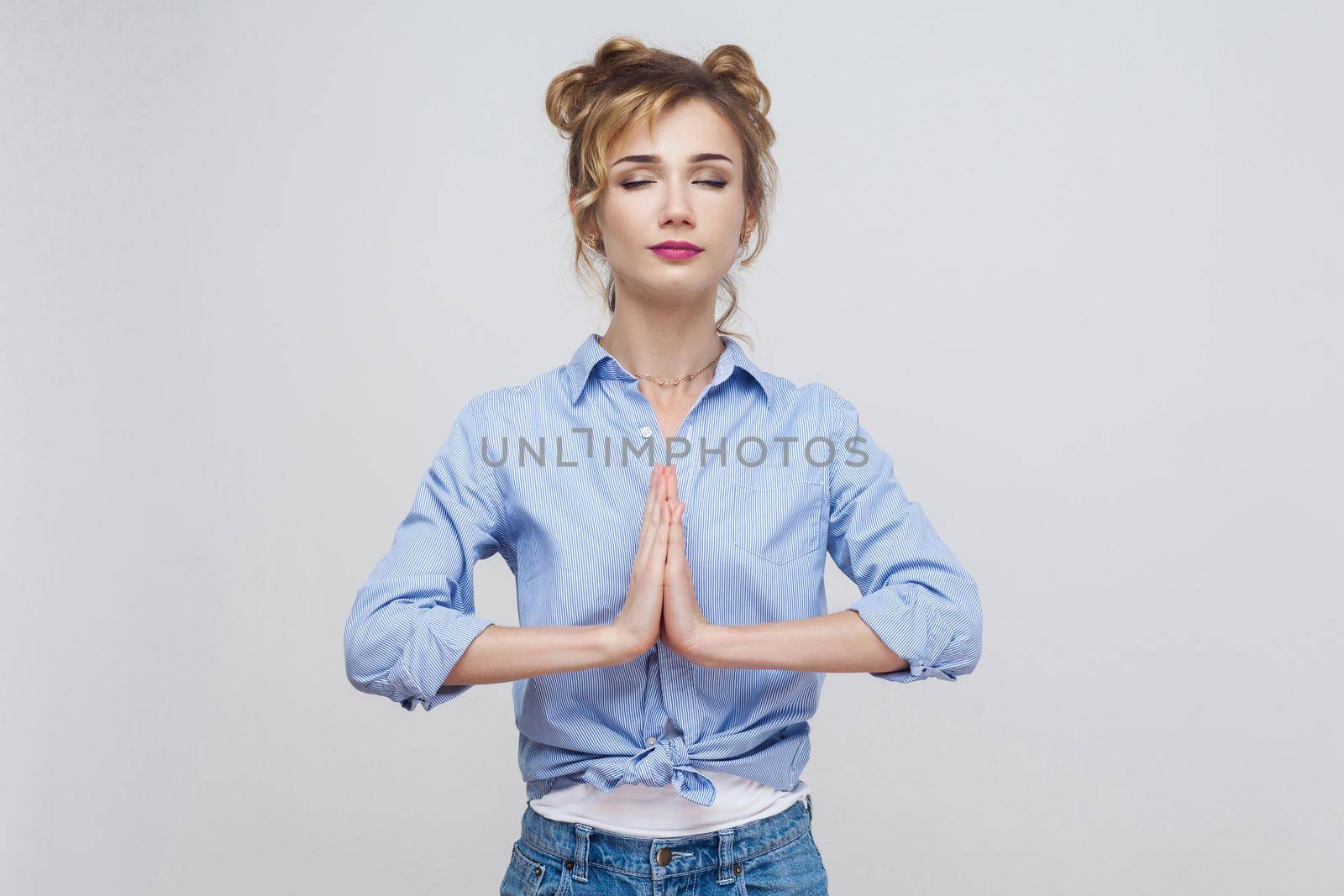 Woman holding hands in namaste or prayer, keeping eyes closed while practising yoga and meditating at home alone, having calm look on her face. Studio shot