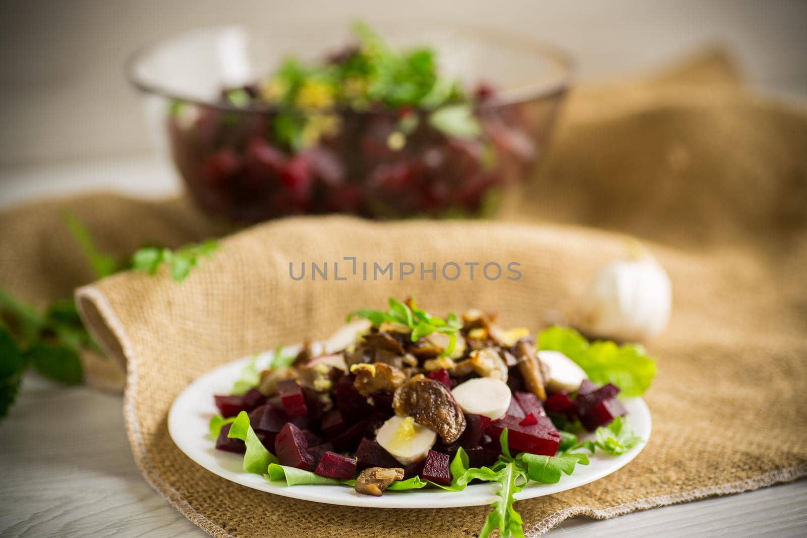 Salad with boiled beets, fried eggplants, herbs and arugula in a plate, on a wooden table.