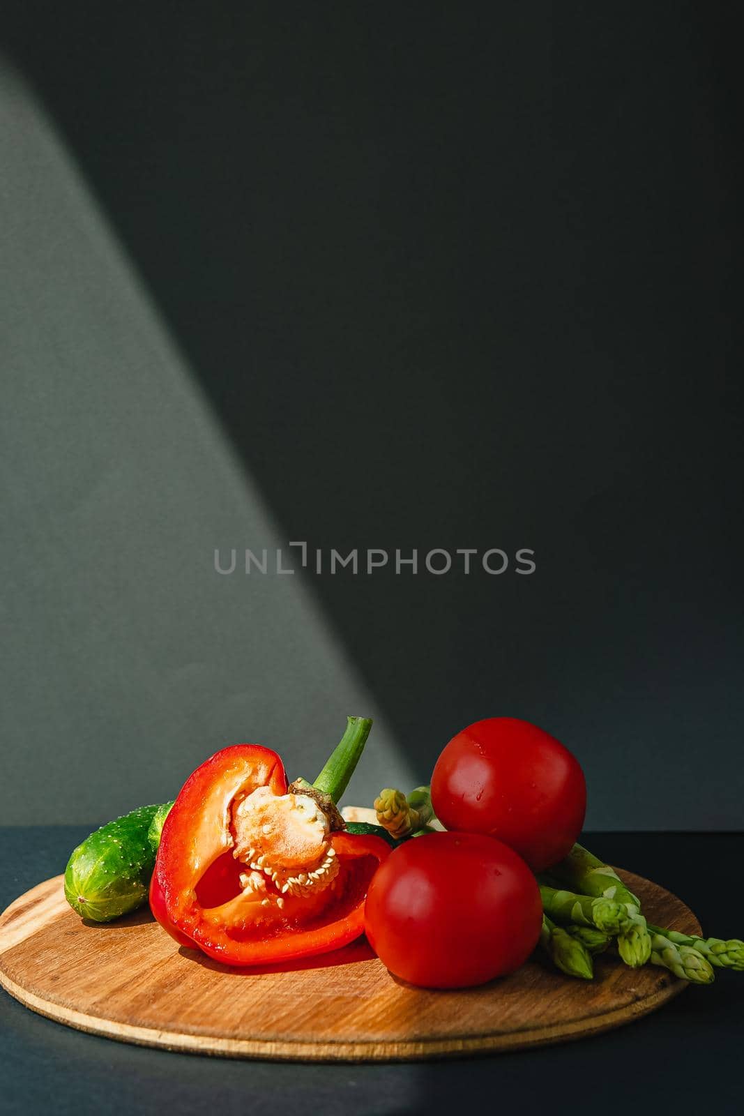 branches of fresh green asparagus, peppers, tomatoes and cucumbers on a wooden board, dark gray background, top view. Basic trend concept with copy space