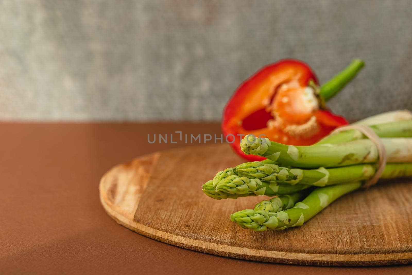 branches of fresh green asparagus on a wooden board, red big pepper on the background. brown background. Basic trend concept with copy space