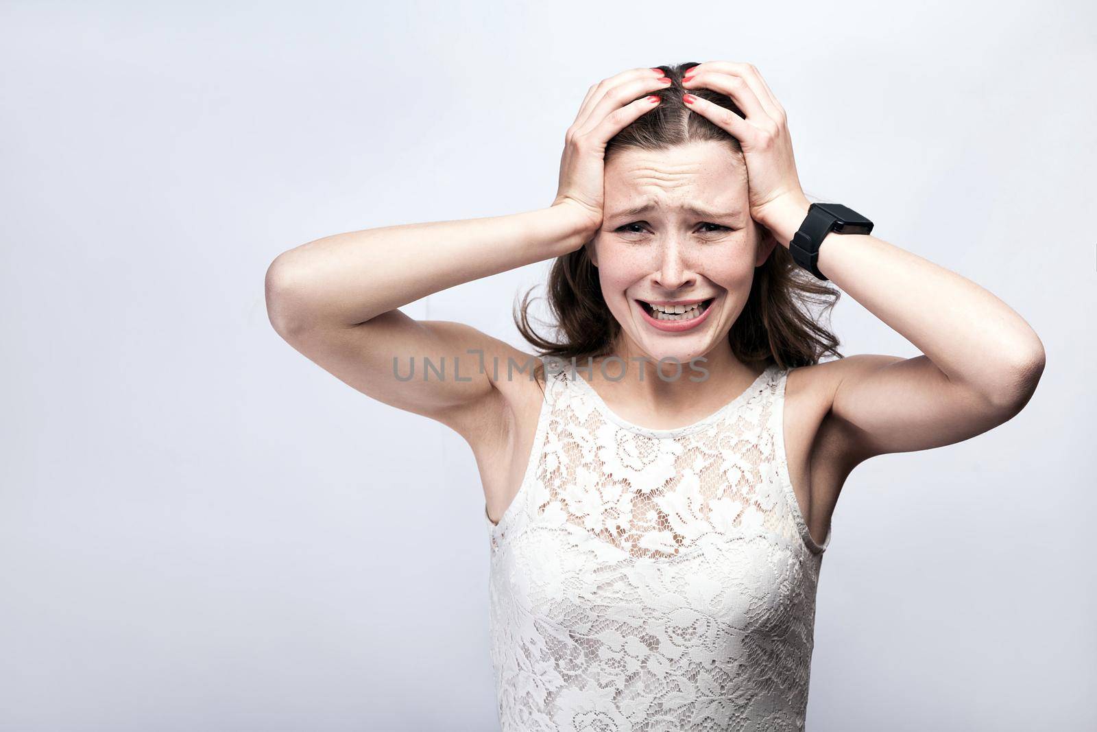 Portrait of beautiful woman with freckles and white dress and smart watch with headache pain on silver gray background. healthcare and medicine concept.