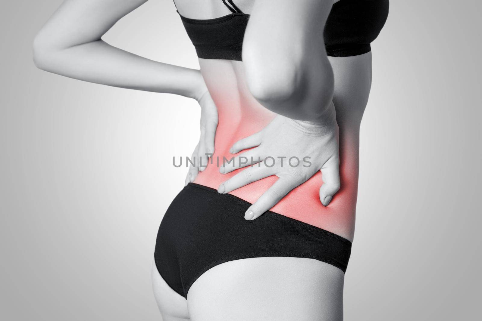 Closeup view of a young woman with pain in back. isolated on white background on gray background. Black and white photo with red dot.