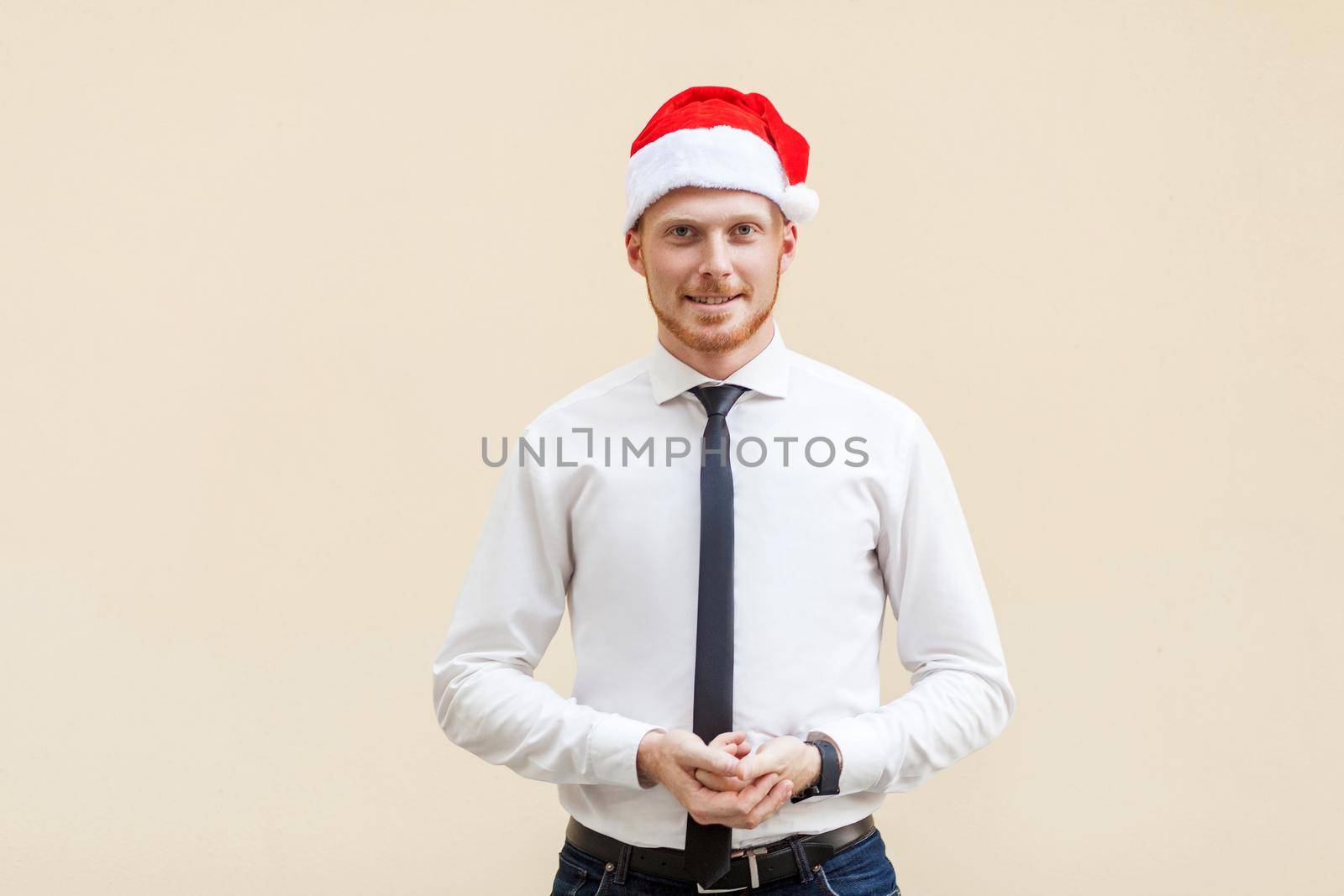 Young adult success ginger businessman looking at camera and smiling. Studio shot, light orange background