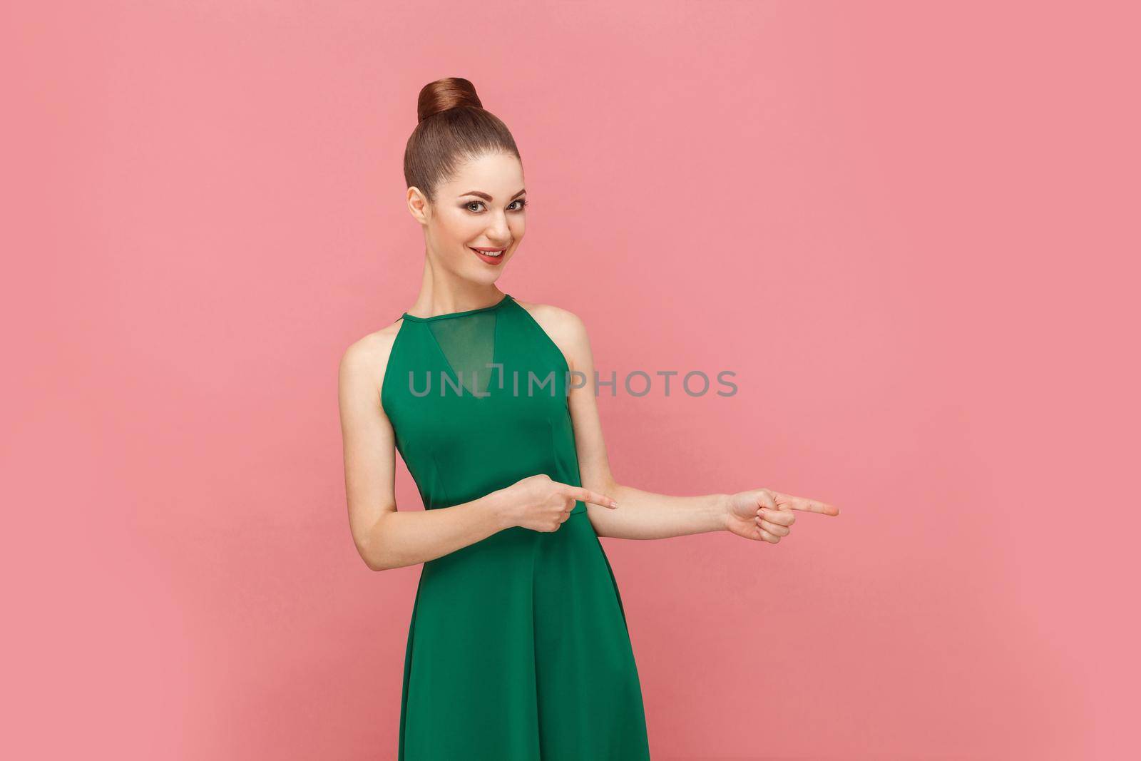 Woman toothy smiling and pointing finger at copy space. Expression emotion and feelings concept. Studio shot, isolated on pink background