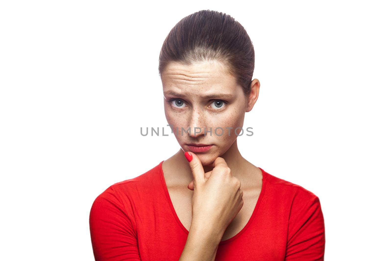 Portrait of thoughtful serious woman in red t-shirt with freckles, studio shot, looking at camera. isolated on white background.