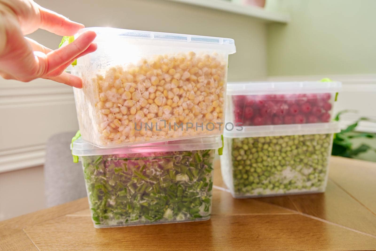 Frozen vegetables and fruits, close-up frozen in the freezer green onions, peas, cherry, corn in plastic containers. Seasonal vegetables, food preparations for the winter