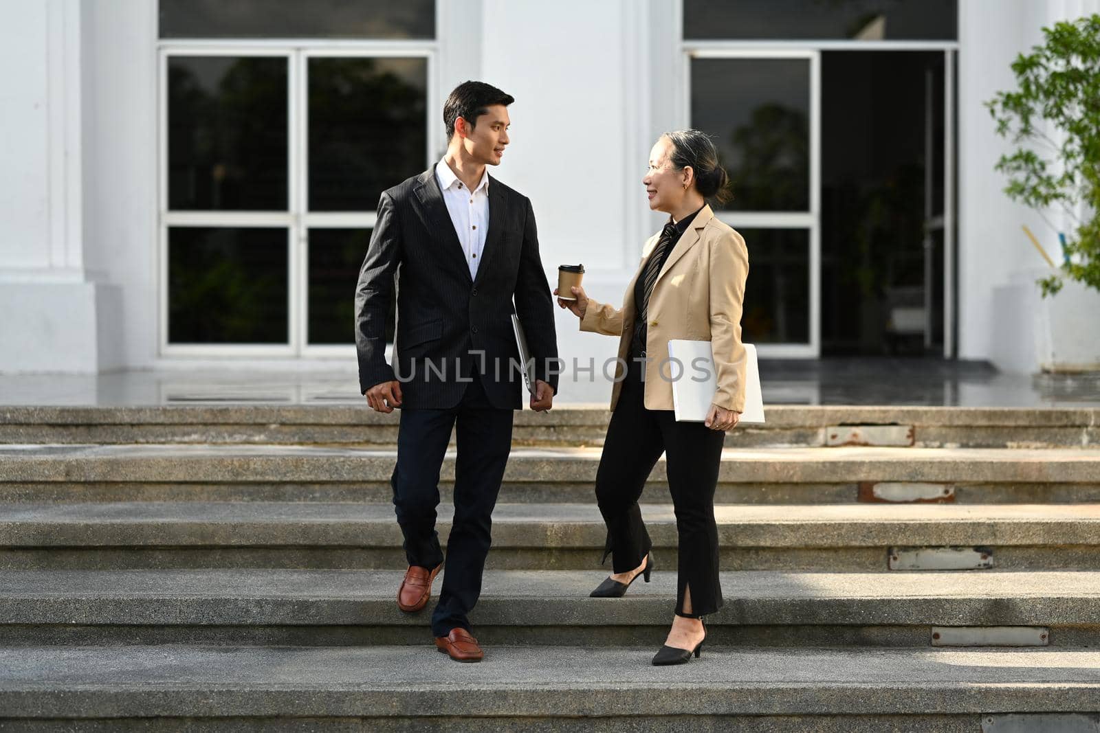 Successful business people having a nice conversation each other and walking down stairs of modern office building by prathanchorruangsak