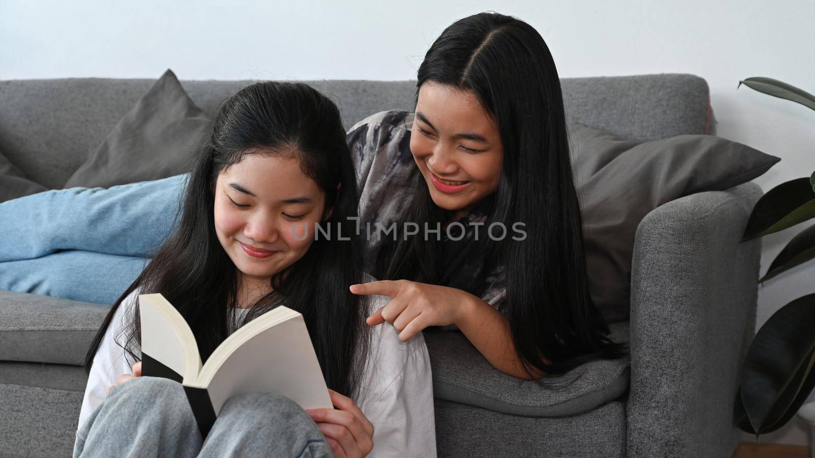 Happy asian girls sitting in living room and reading book together. by prathanchorruangsak