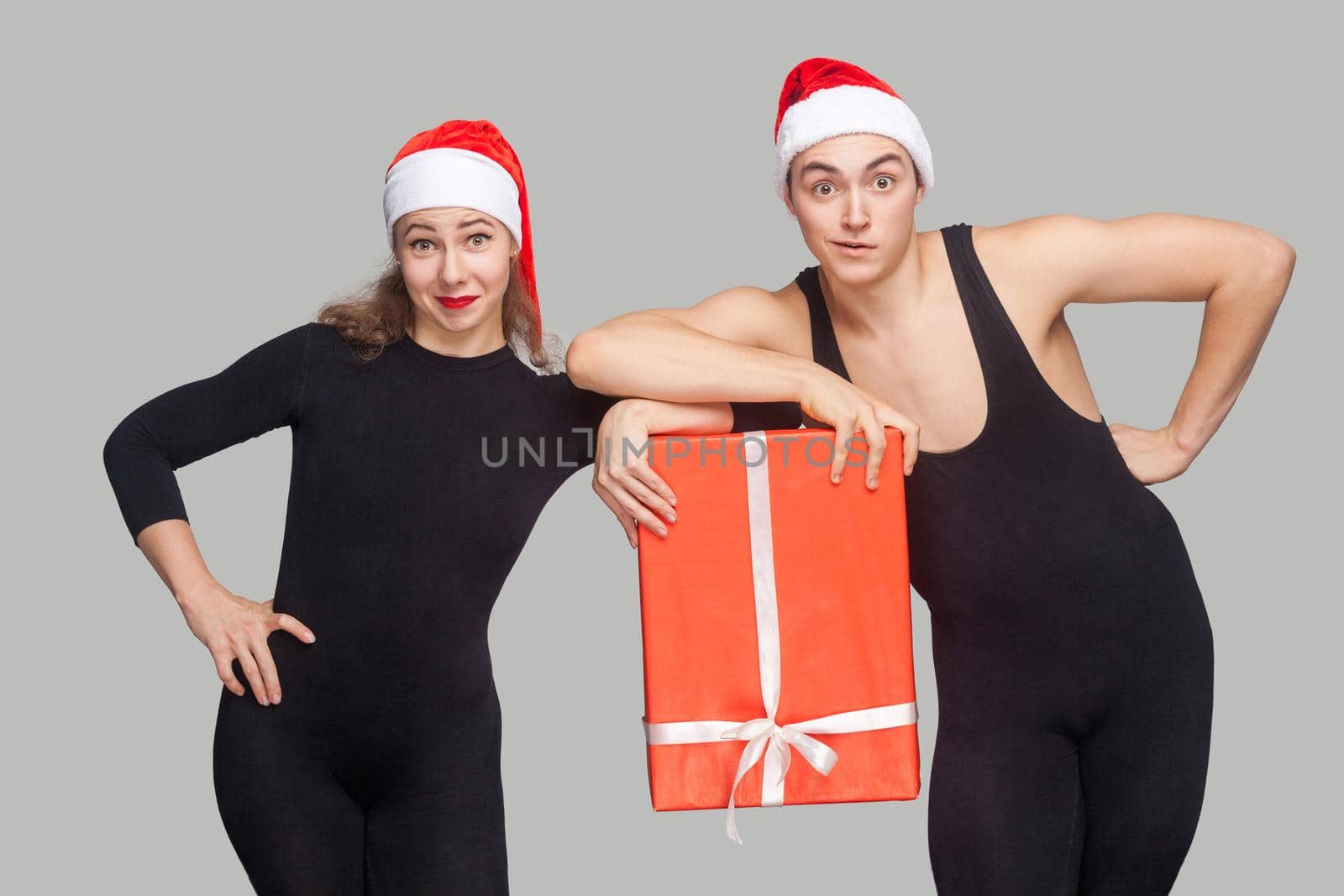 funny couple in black dress and red christmas hat holding gift box together and looking at camera. by Khosro1