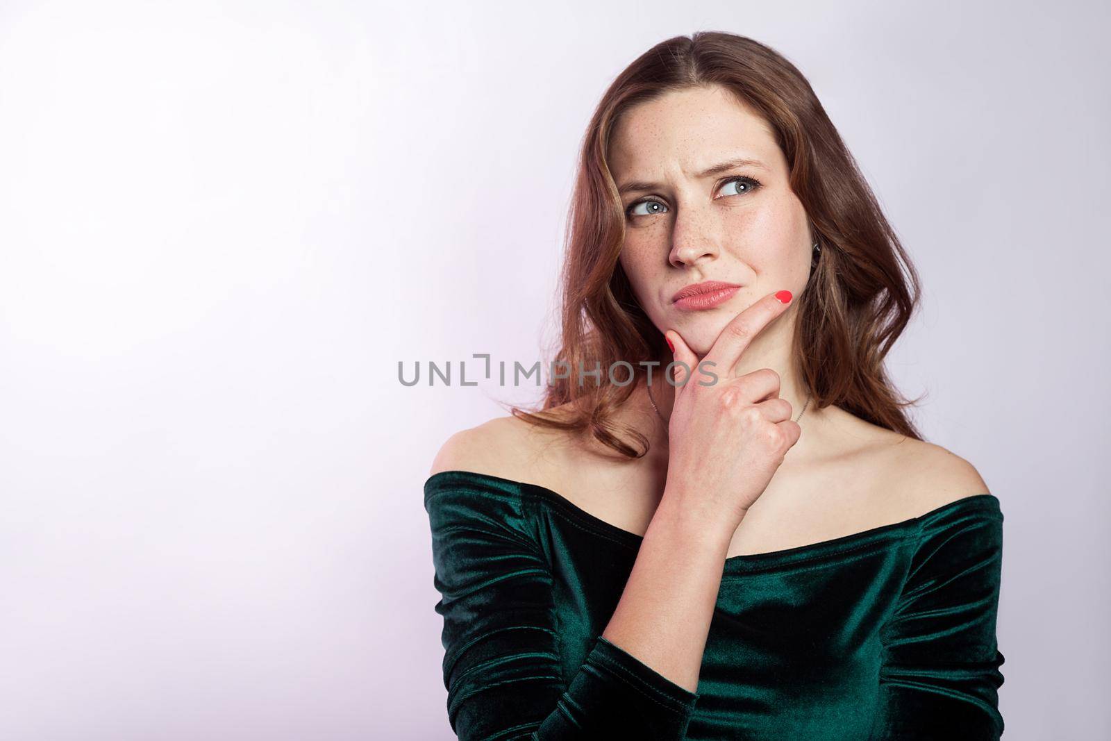 Portrait of thinkful woman with freckles and classic green dress. studio shot on silver gray background.