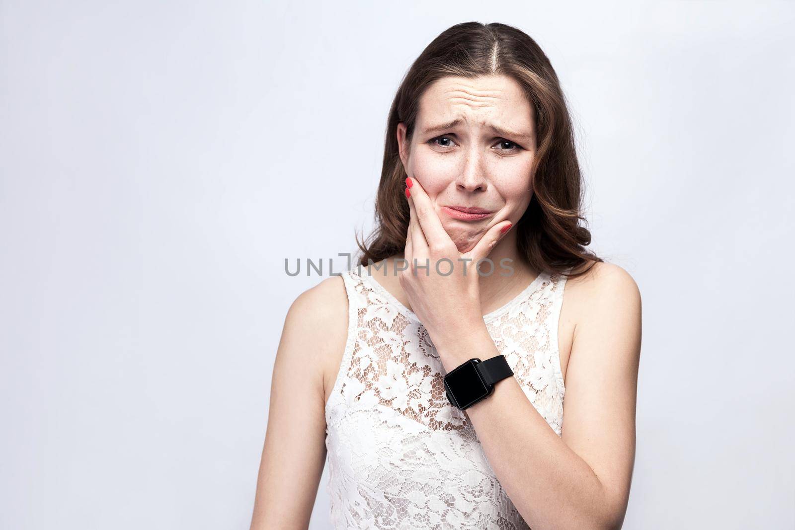 Portrait of beautiful woman with freckles and white dress and smart watch with tooth pain on silver gray background. healthcare and medicine concept.