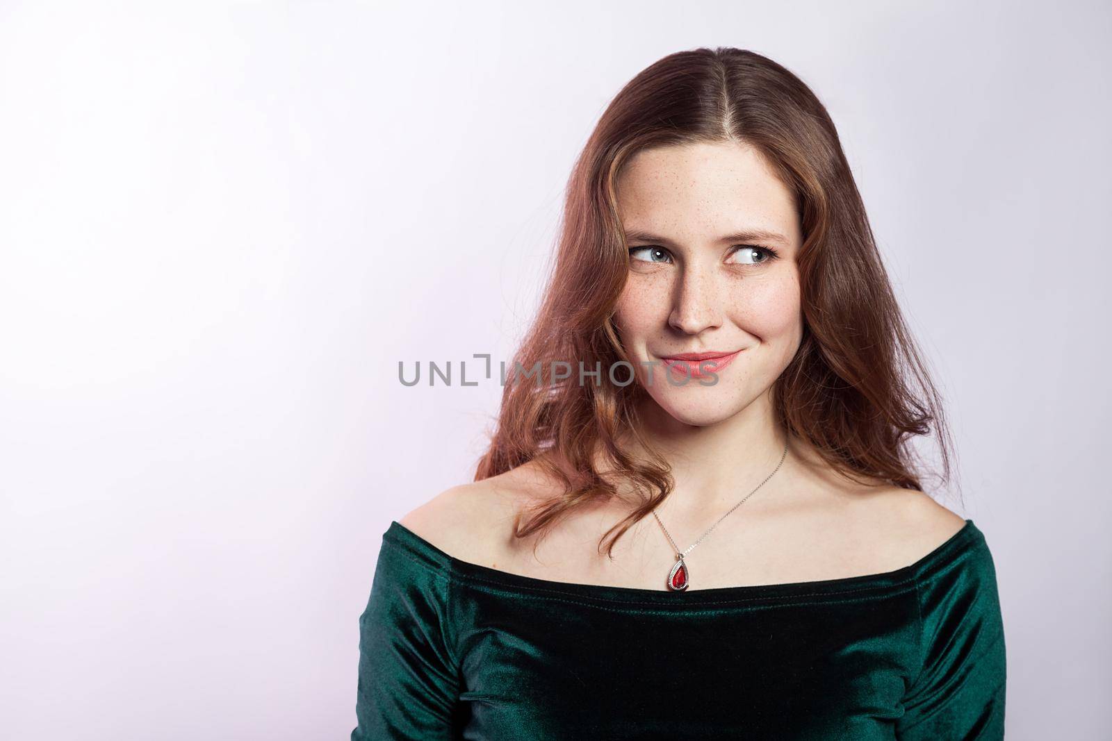Portrait of thinkful woman with freckles and classic green dress. studio shot on silver gray background.