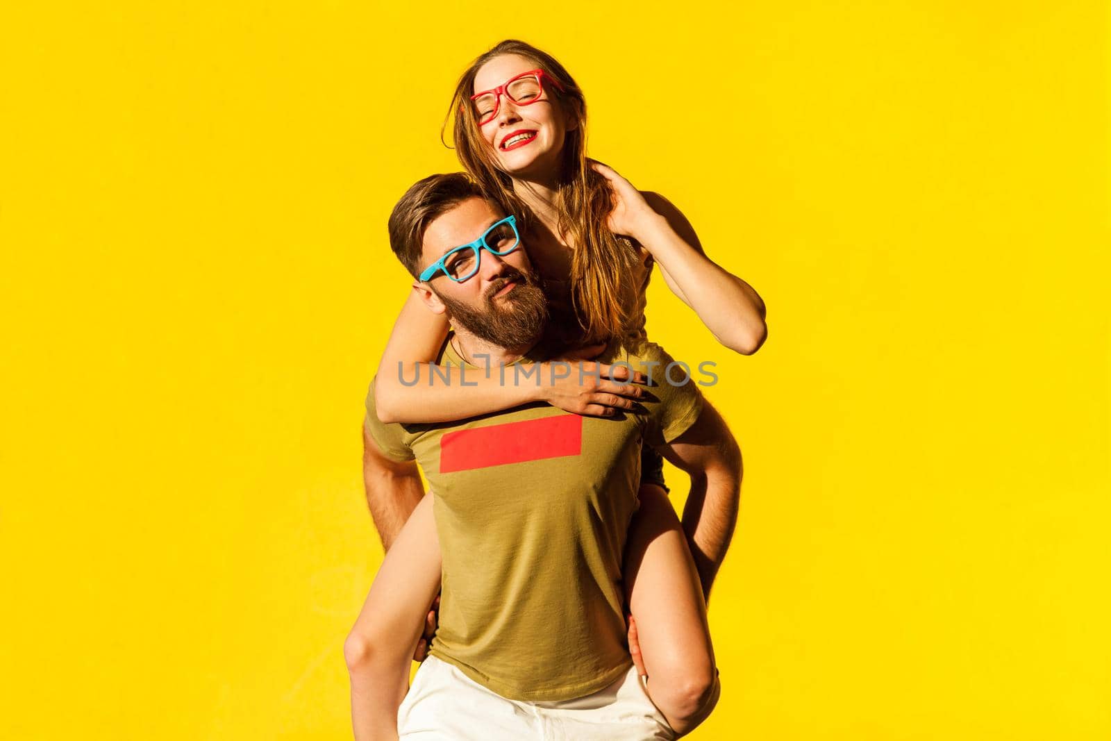 Piggyback. Happiness friend looking at camera and posing on yellow background. Studio shot