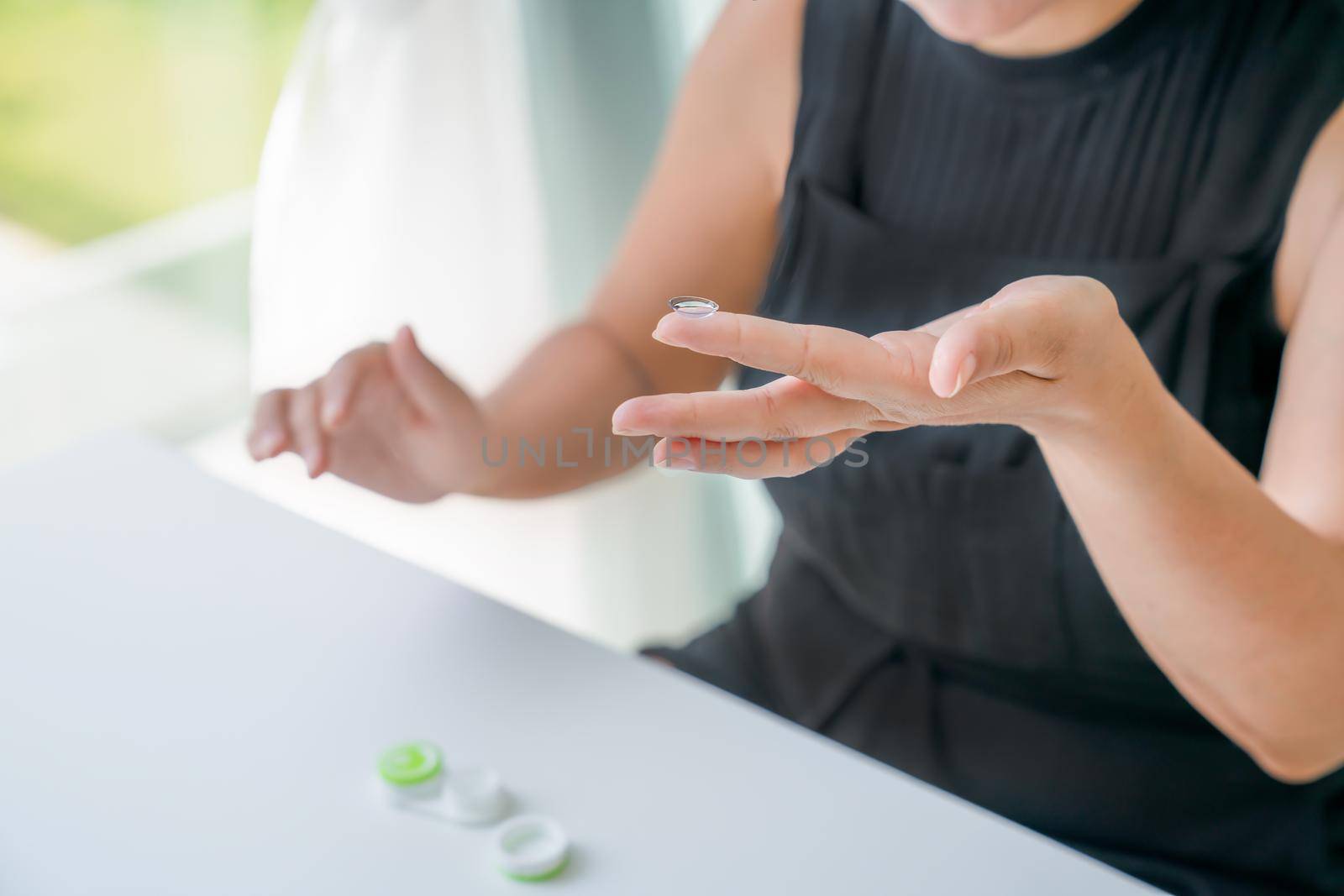 Contact lens is on girl's index finger. There is container for lenses nearby. Close-up, side view