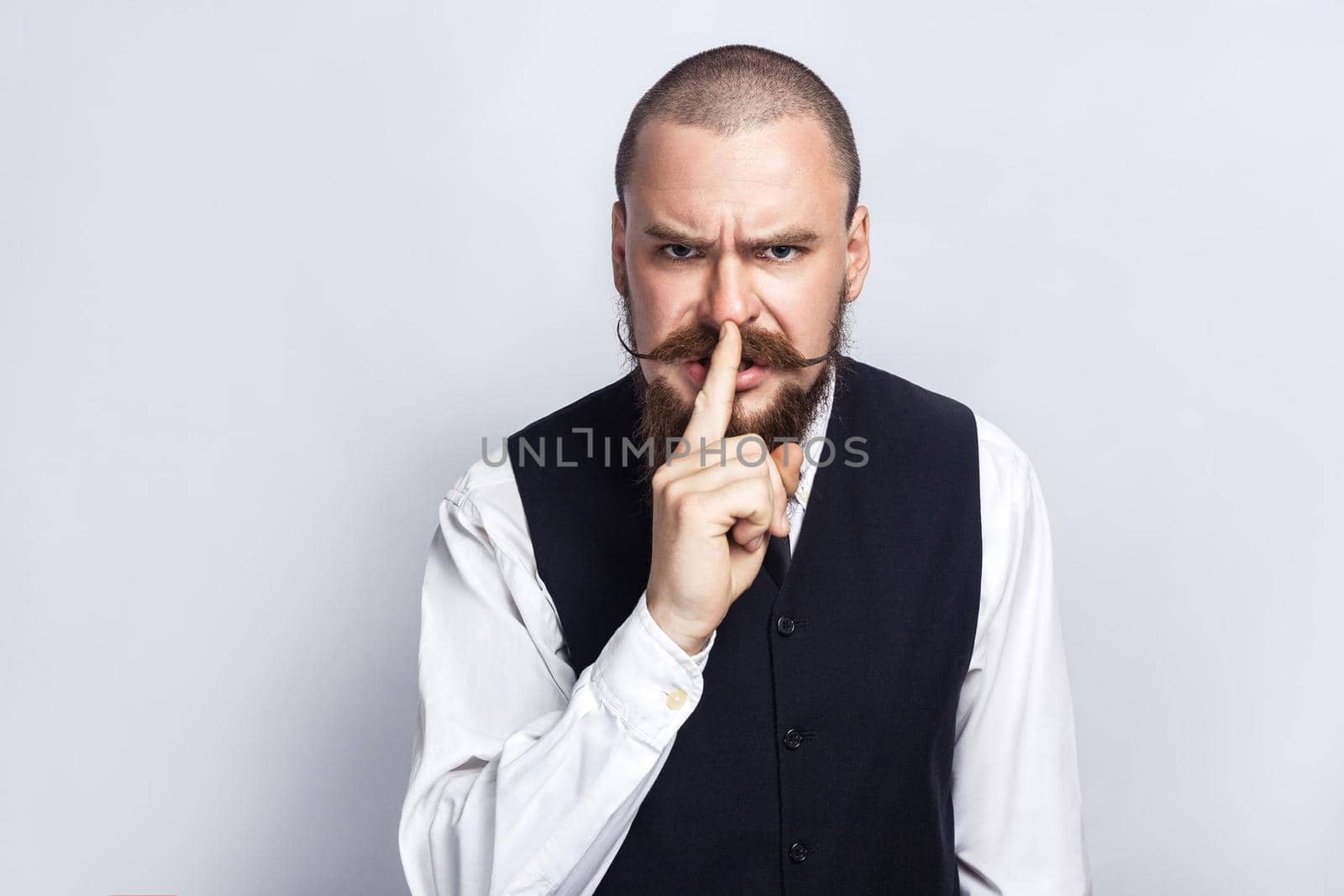 Shh, Handsome businessman with beard and handlebar mustache looking at camera with silent sing. studio shot, on gray background.