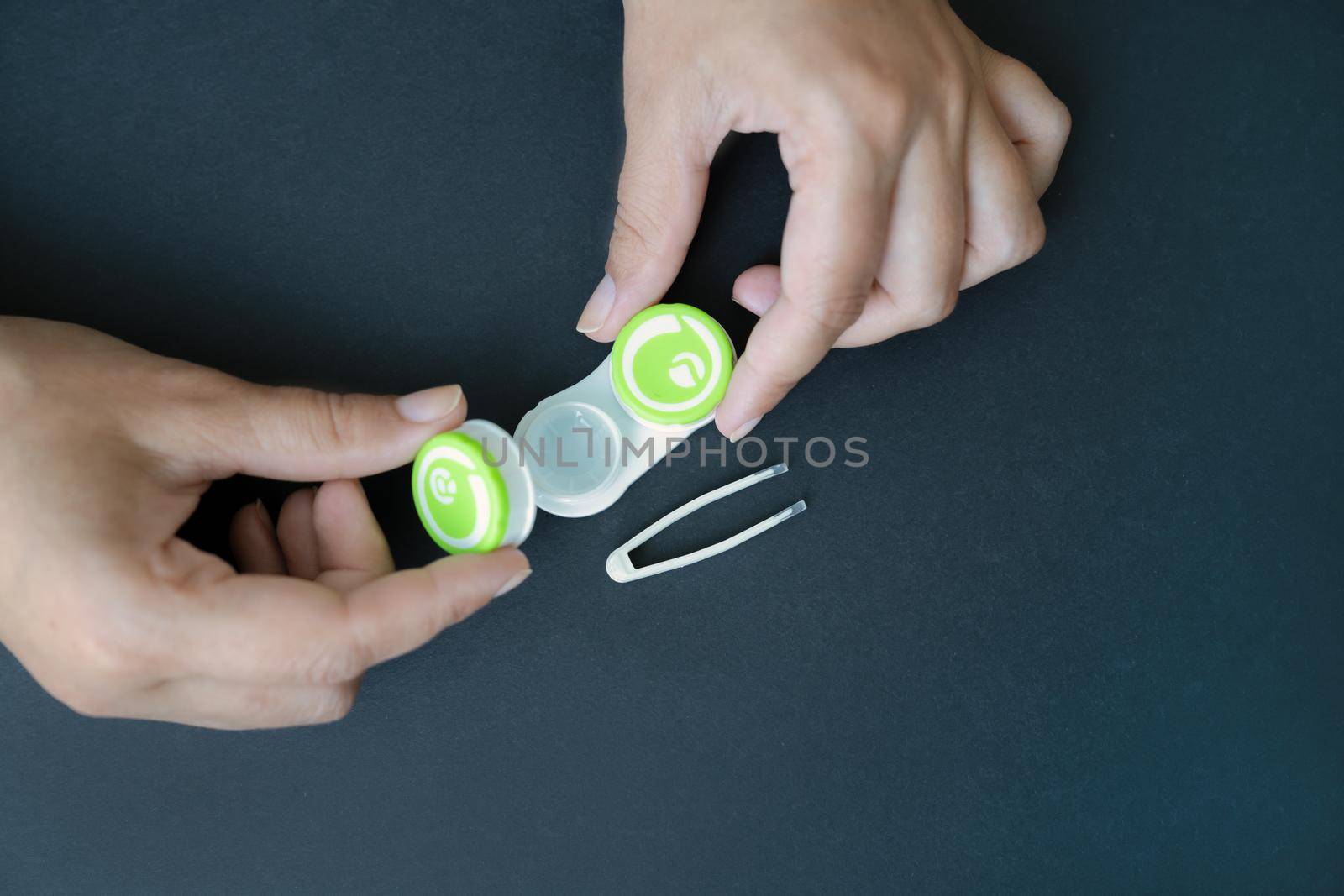 Girl opens container with lenses. Pair of tweezers for lenses lies next to it on a black background. Close-up, top view, copy space