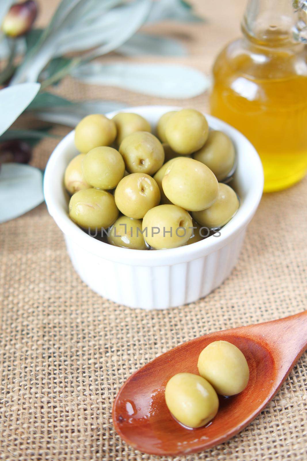 bottle of olive oil and fresh olive in a container on table