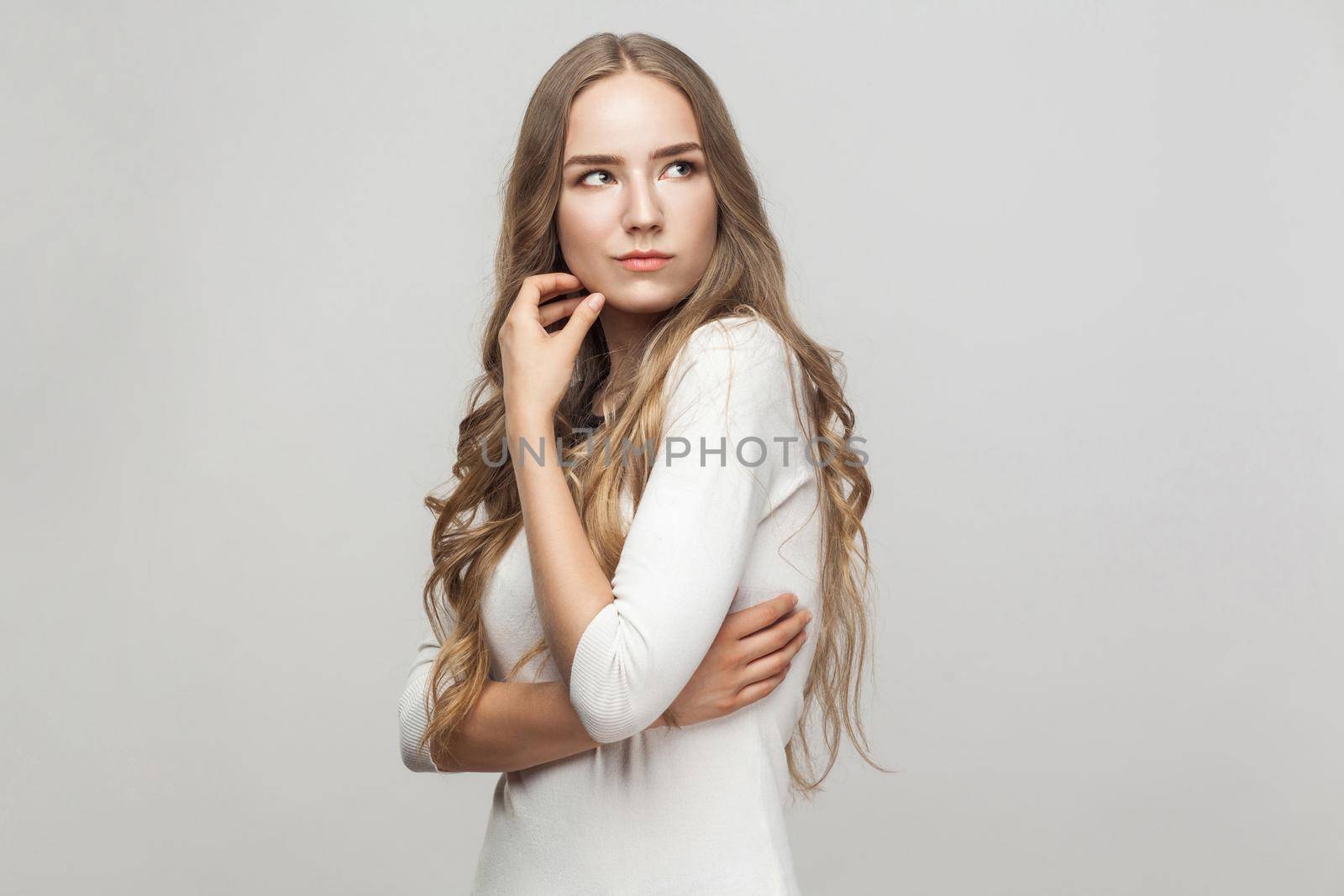 Pondering woman touching her face and looking up. Studio shot, gray background