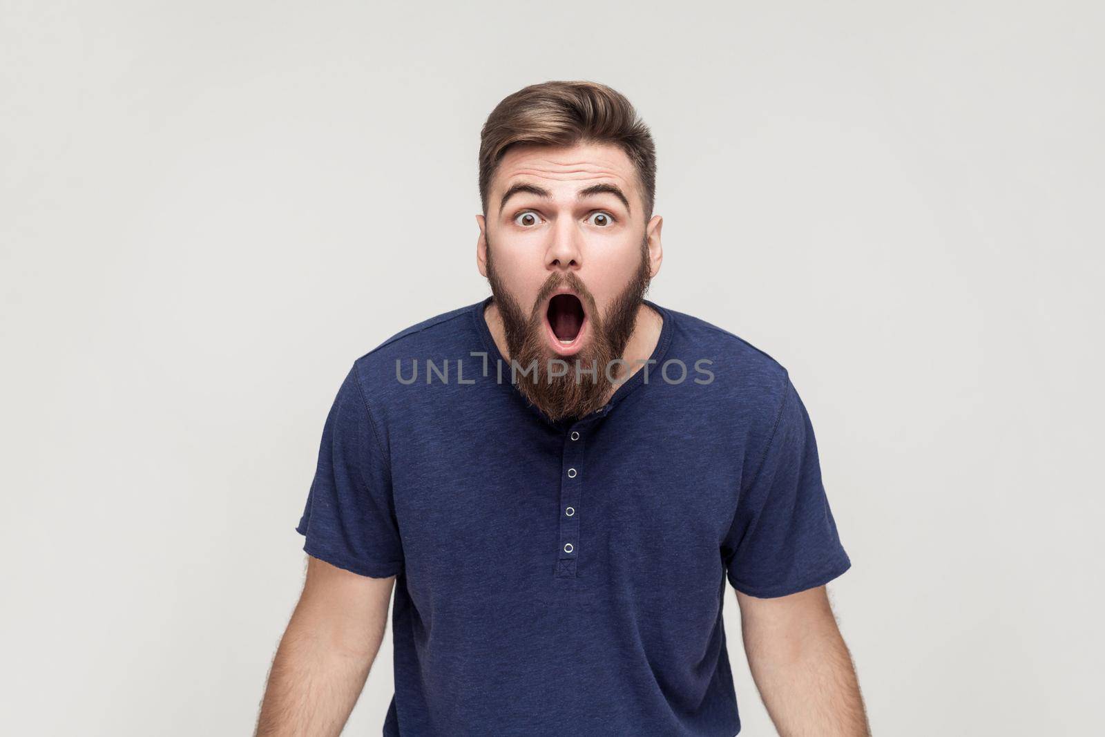 Unbelievable news! Young adult crazy man with opened mouth looking at camera. Studio shot, gray background