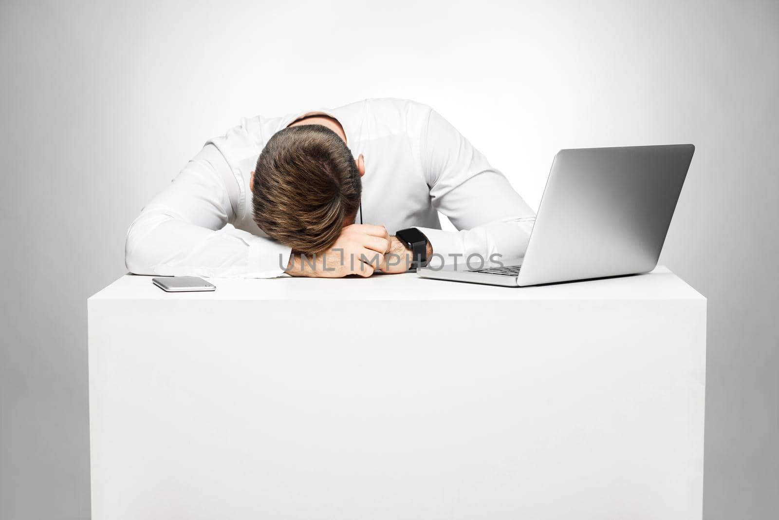 Sweet dreams tired in the work station. Portrait of sleepy tired freelancer in white shirt are sitting in office is snoozing at his work place near laptop. Indoor, studio, gray background, isolated