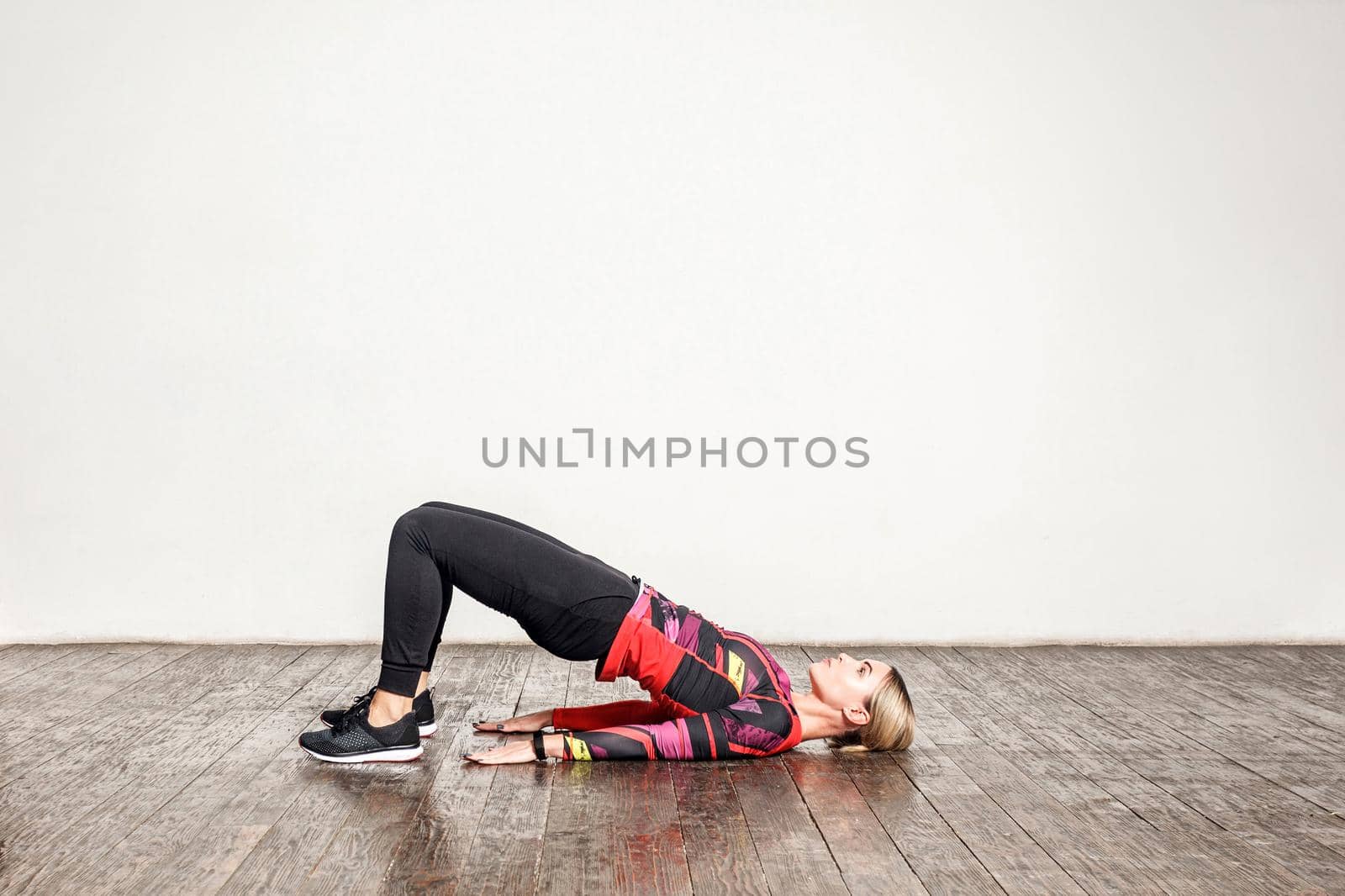 Athletic woman in tight sportswear practicing yoga, doing bridge pose bending back, stretching body, training flexibility, muscle strength. Health care and sports activity at home. indoor studio shot