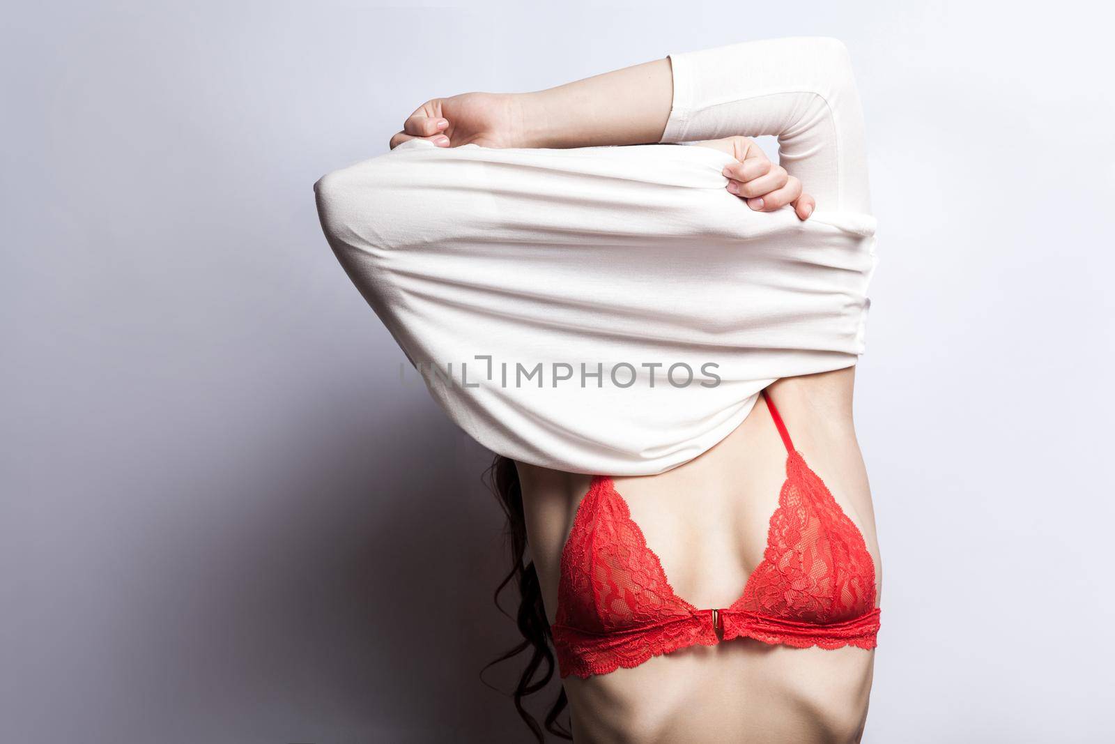 Sexy model posing and undressing at camera. Studio shot. Gray background
