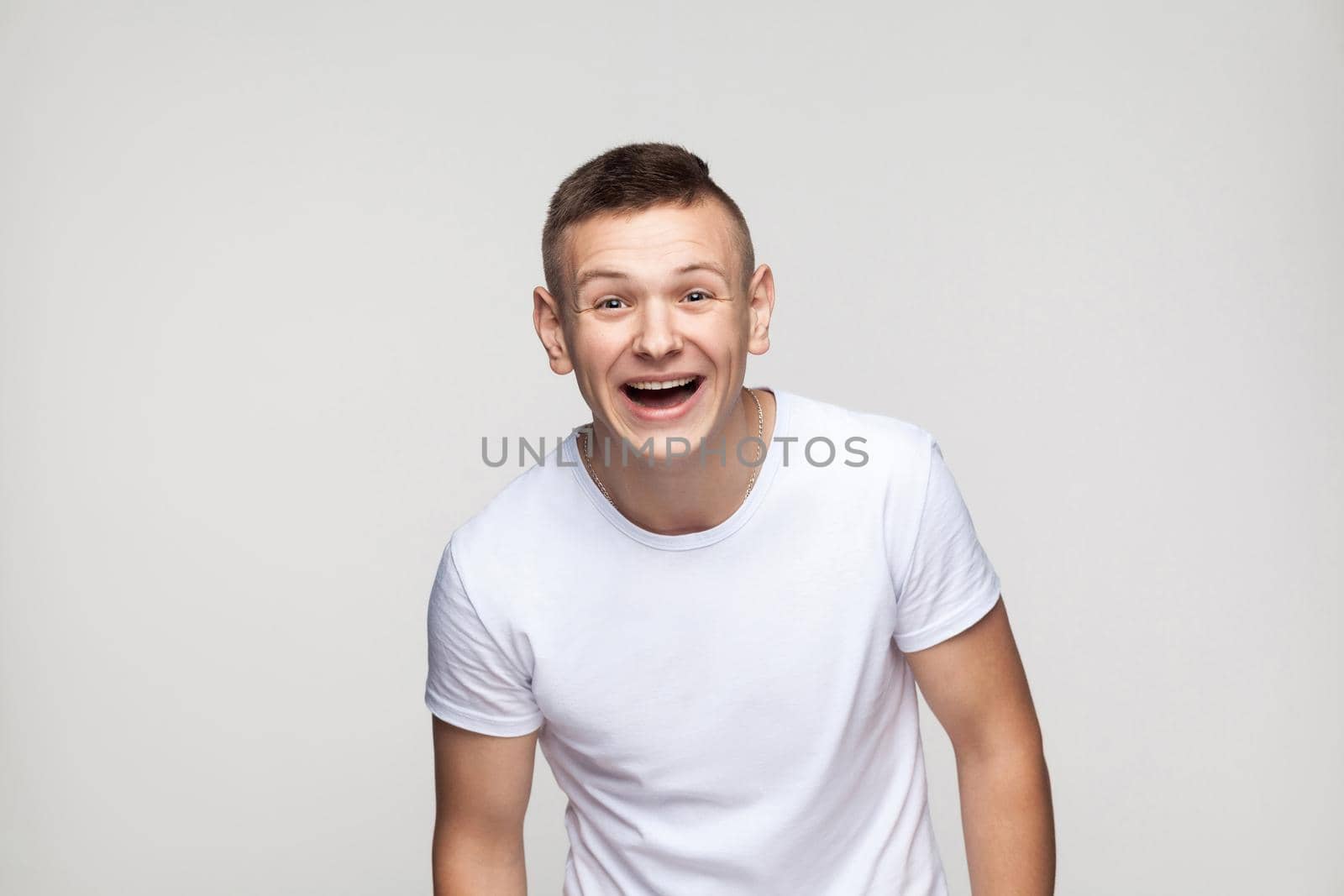 Young success man looking at camera and toothy smile. Studio shot, gray background