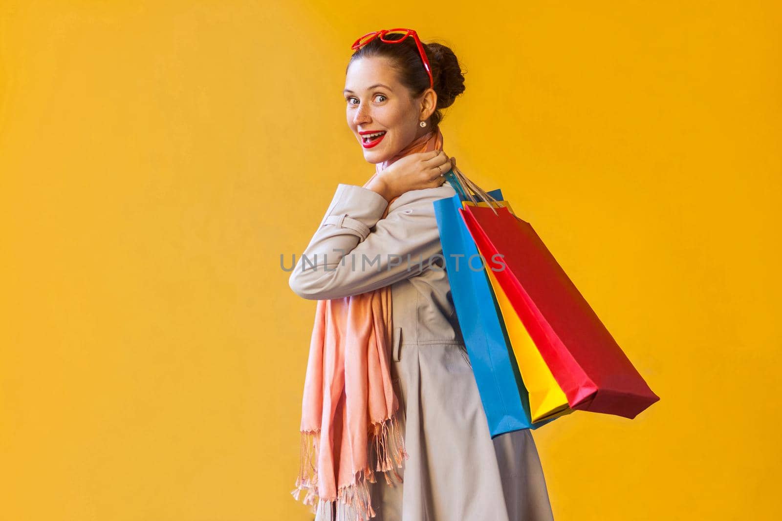 Profile, side view beautiful and happiness shopaholic girl with many packets. Looking at camera and smiling. Studio shot, yellow wall