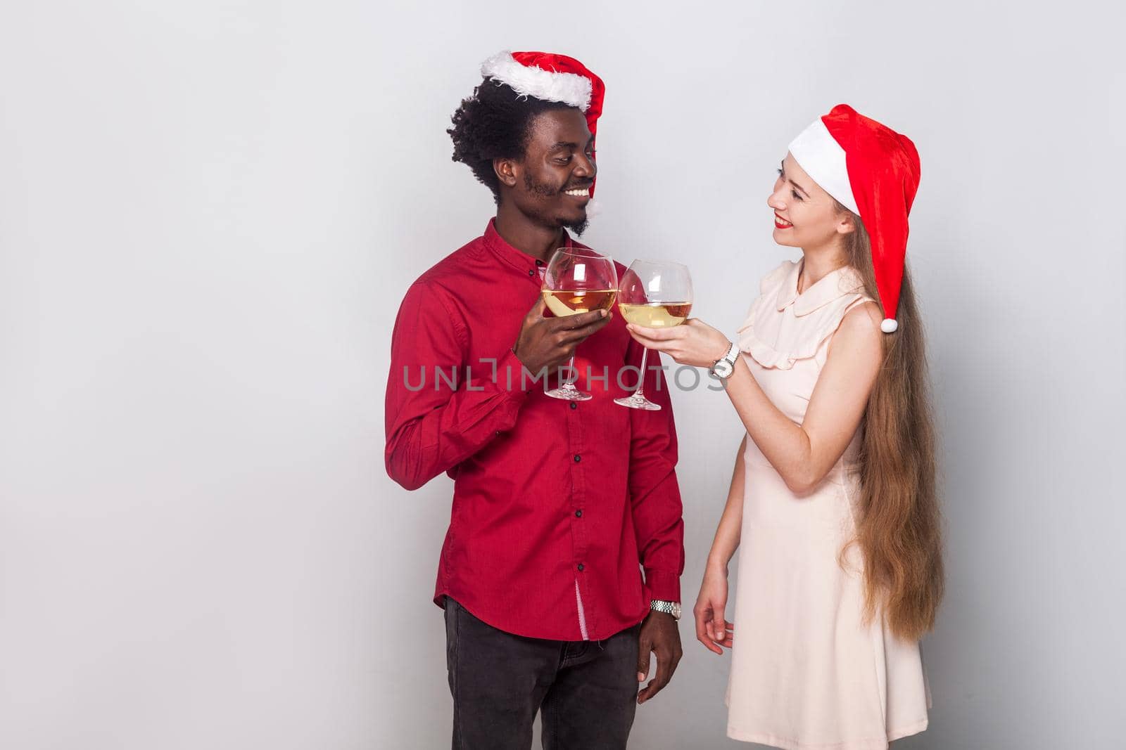 Flirt and love concept. Man and young adult woman in christmas cap, holding glasses with champagne and looking each other with love. Indoor shot