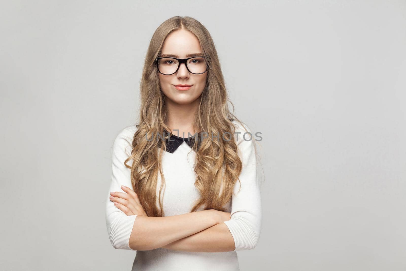Woman in formal wear crossed hands, toothy smiling and looking at camera. Studio shot, gray background