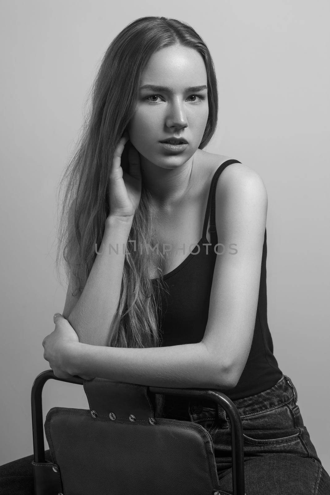 Beautiful woman sit on chair and touching her long hair. Studio shot, isolated on gray background