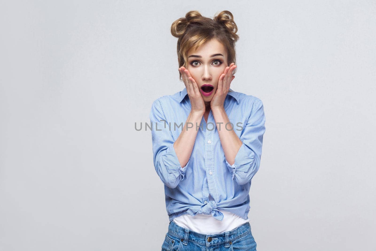Human face expressions and emotions. Blonde woman screaming with shock, holding hands on her cheeks. Isolated studio shot on gray background.