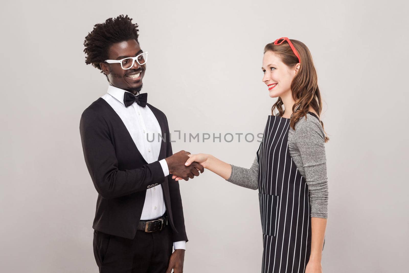 African man and freckles caucasian woman handshake and toothy smiling. Studio shot