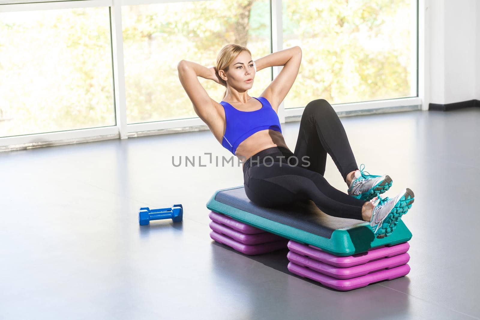 Blonde woman lie on step platform and doing press aerobic. Studio shot