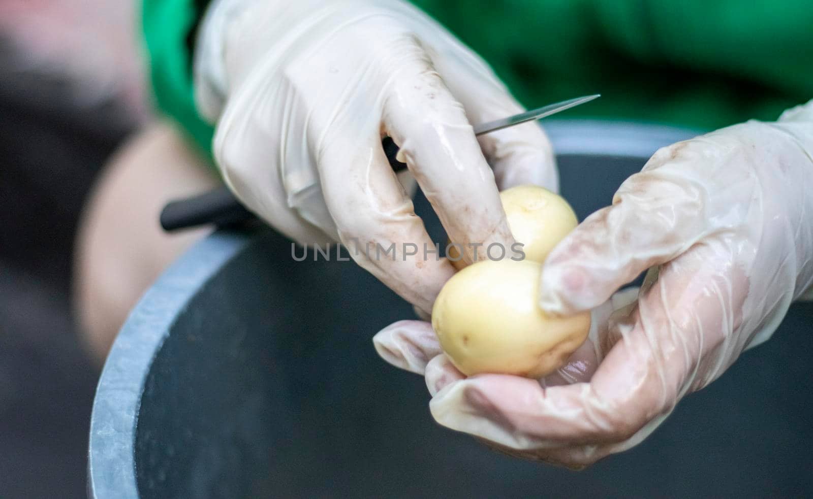 Woman's hands in white gloves peel raw new potatoes, close-up. Cleaning organic potatoes. Detail of female hands peeling fresh yellow potato with kitchen knife, food preparation concept