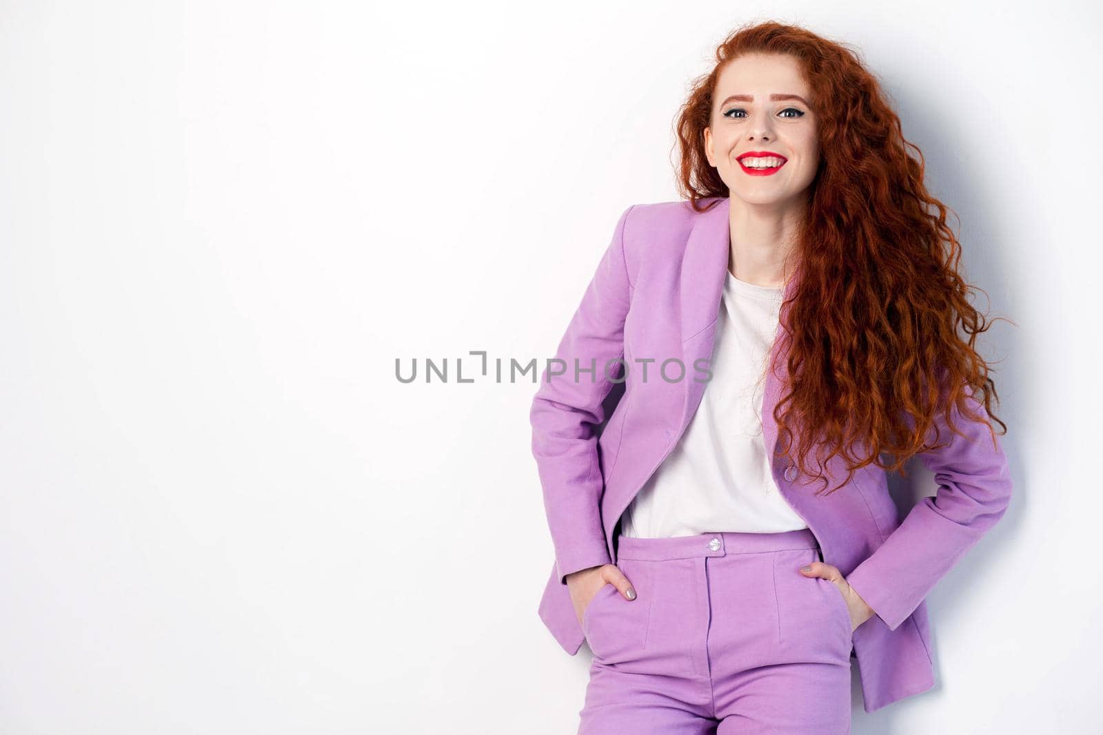 Portrait of successful happy beautiful business woman with red - brown hair and makeup in pink suit. looking at camera with toothy smile, studio shot on gray background.